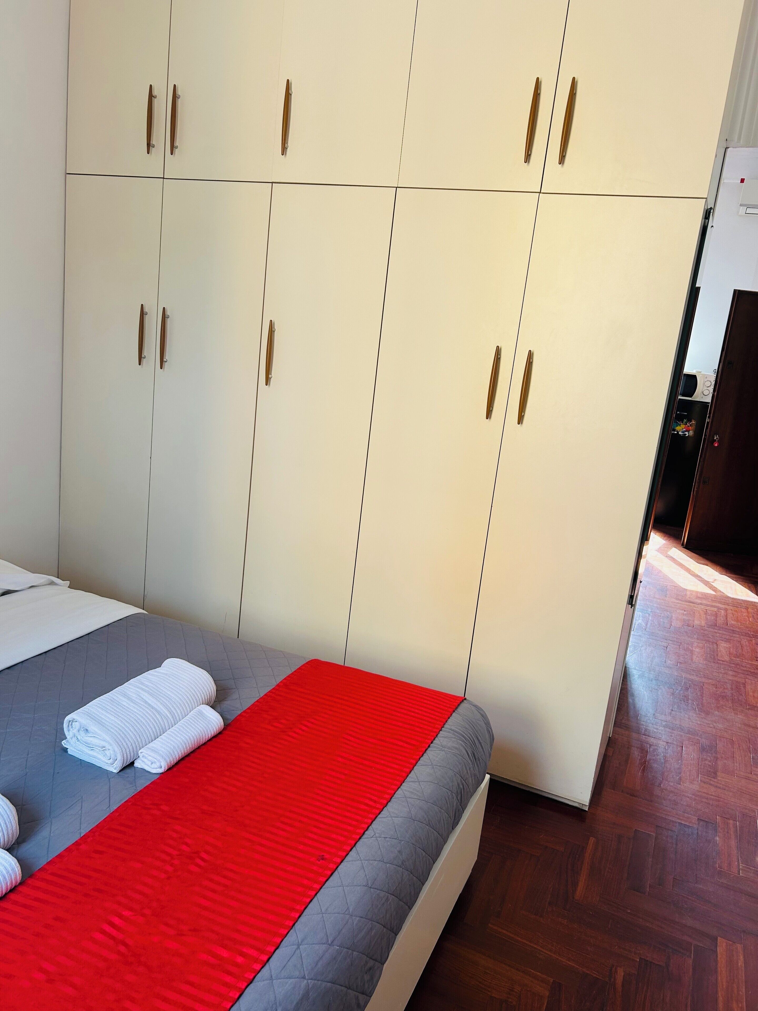 Una habitación de hotel con una cama, un edredón rojo y un armario con varias puertas.