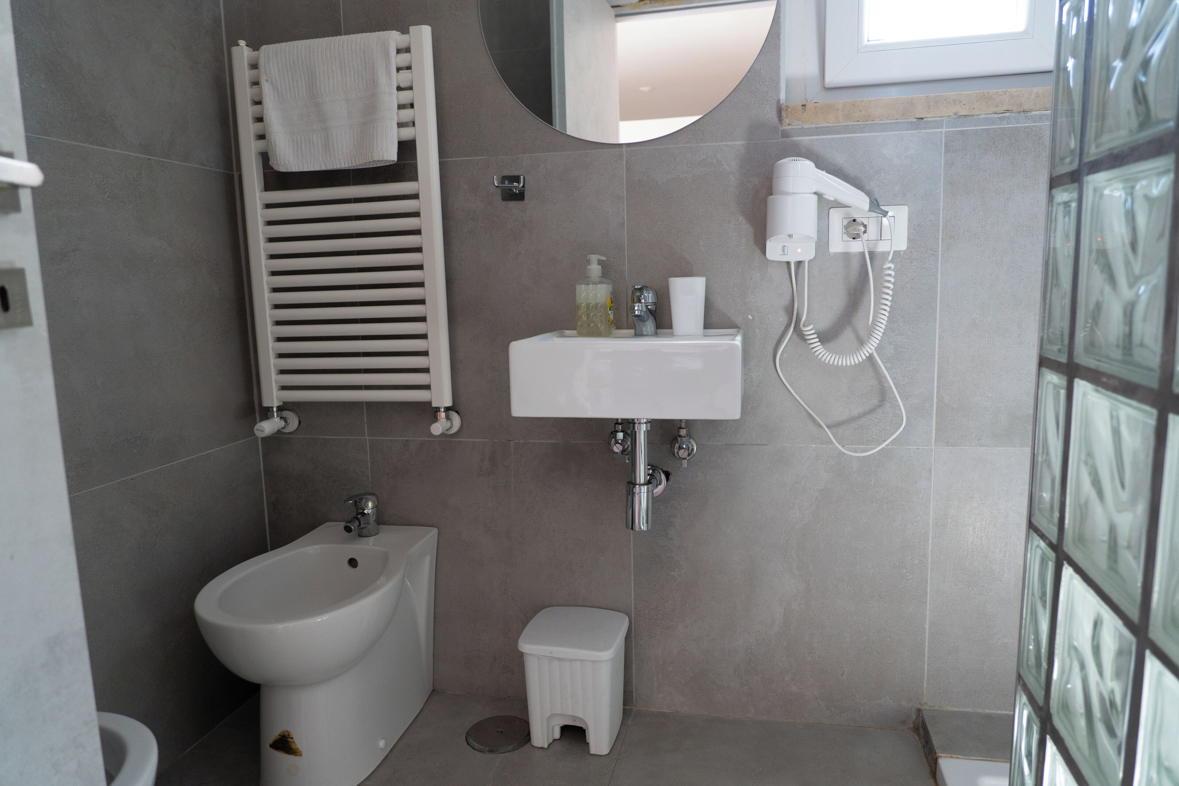 Une salle de bain moderne équipée d’un bidet, d’un petit tabouret, d’un porte-serviettes, d’un lavabo et d’une douchette à main.