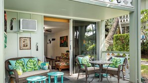 Een overdekt terras met rieten meubels en een tafel, omringd door een witte hek en groen.