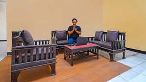 A person sitting on a sofa with a laptop in a room with wooden furniture and a tiled floor. - OYO Life 92641 Guest House Palinggihan Ii (Sumber)