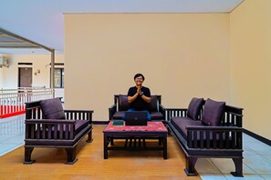 A person sitting on a dark-colored sofa in a room with a tiled floor and a plain wall. - OYO Life 92641 Guest House Palinggihan Ii (Sumber)