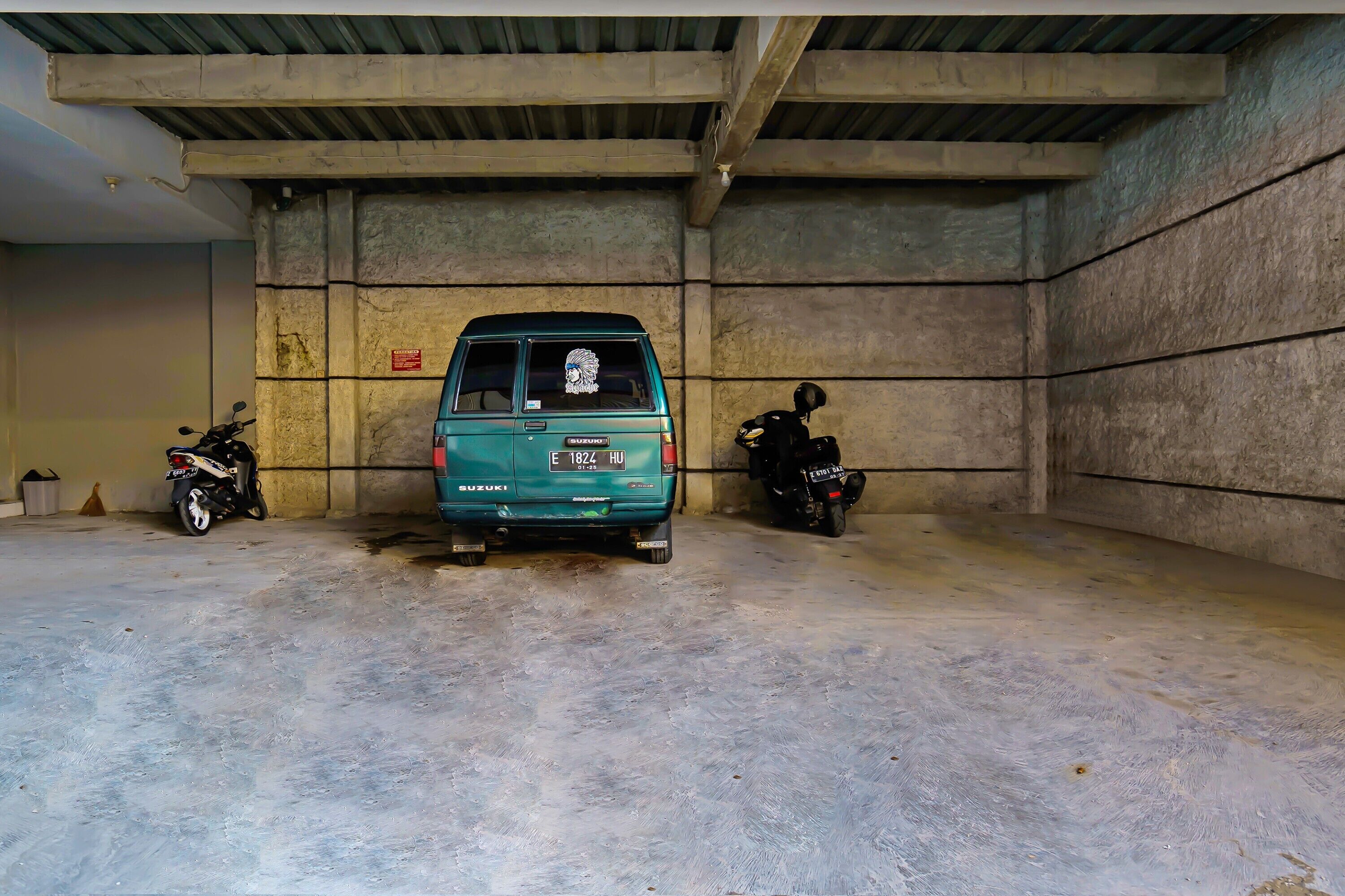 A parking garage with a teal van and two motorcycles parked inside.