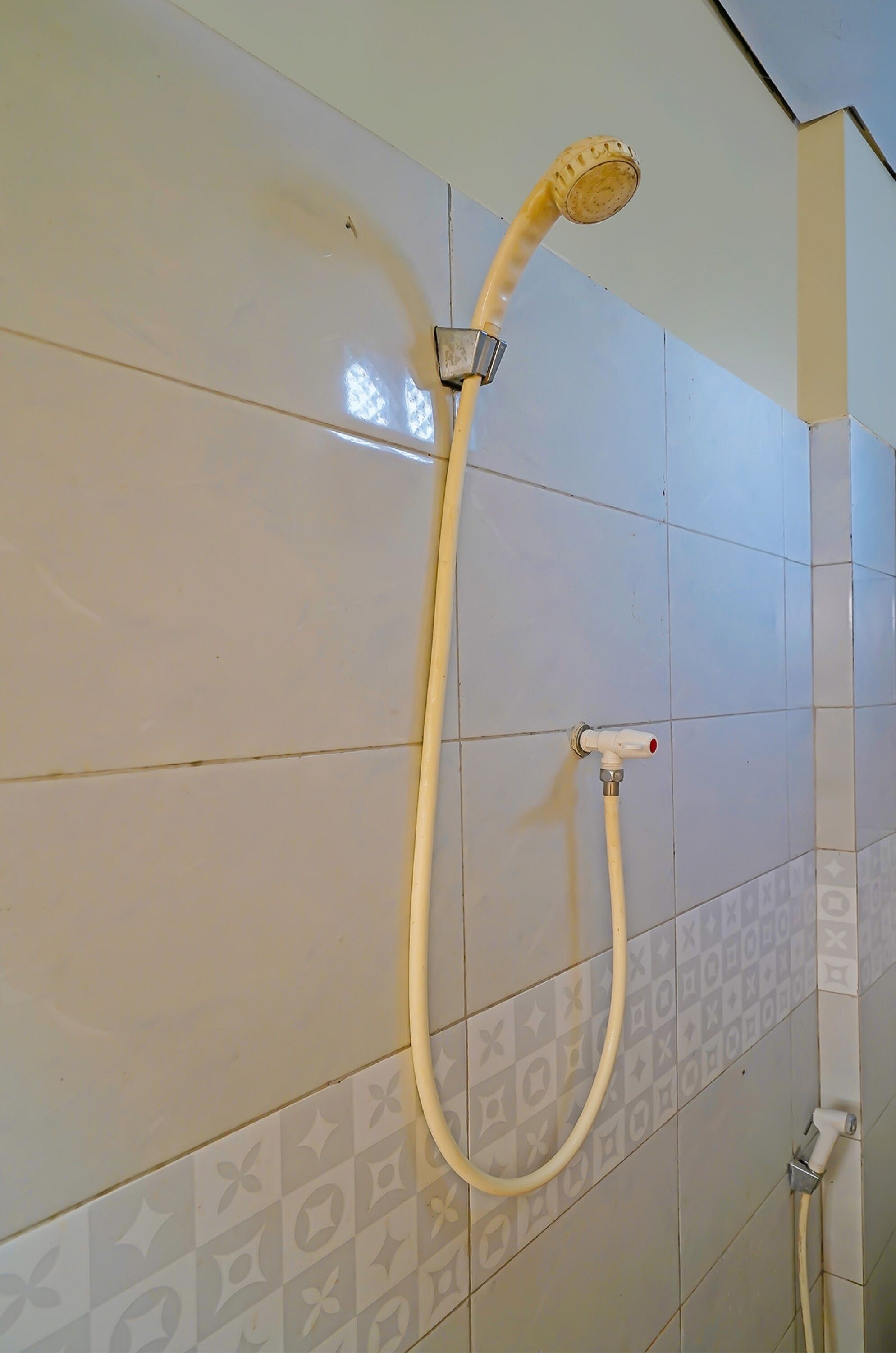 Douche met een handdouche en een flexibele slang, bevestigd aan een betegelde wand met een geometrisch patroon.