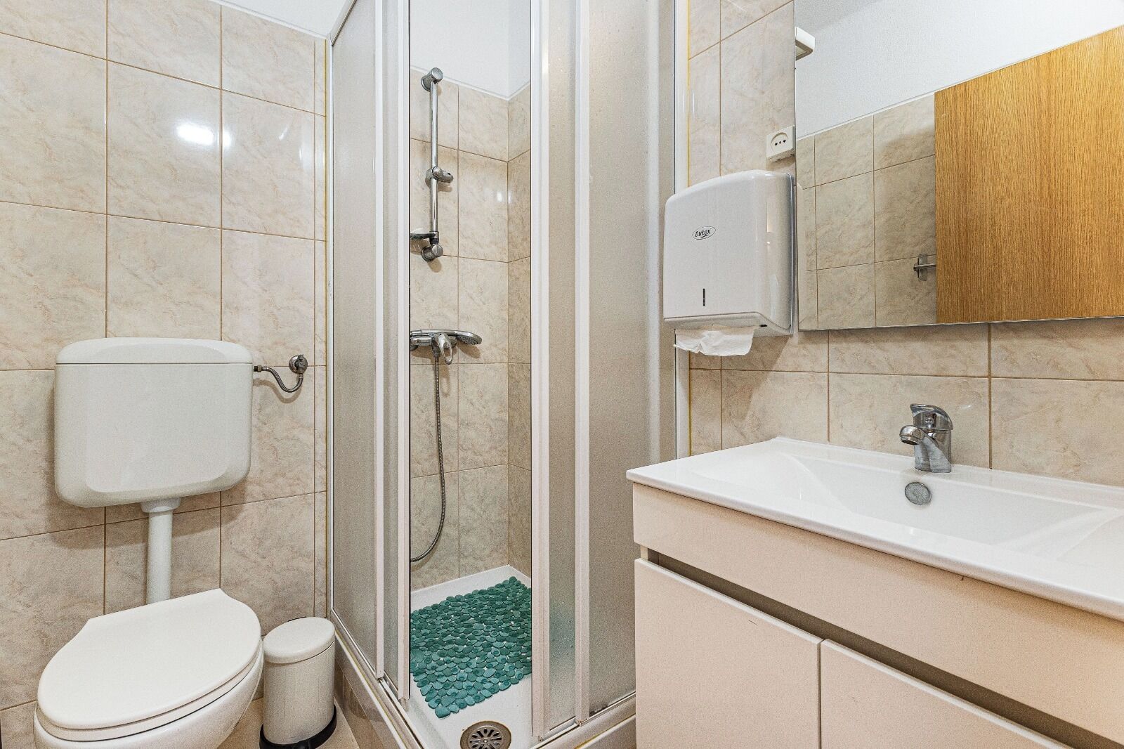 A bathroom with a toilet, shower, sink, and a mirror.
