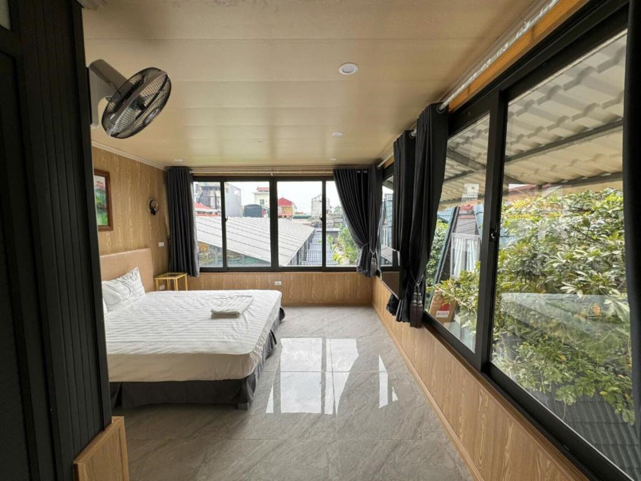 Ein Schlafzimmer mit einem Bett, einem Ventilator und einem großen Fenster mit Vorhängen.