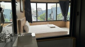 Ein Hotelzimmer mit Bett, großem Fenster und einem Badezimmer mit Waschbecken und Spiegel.
