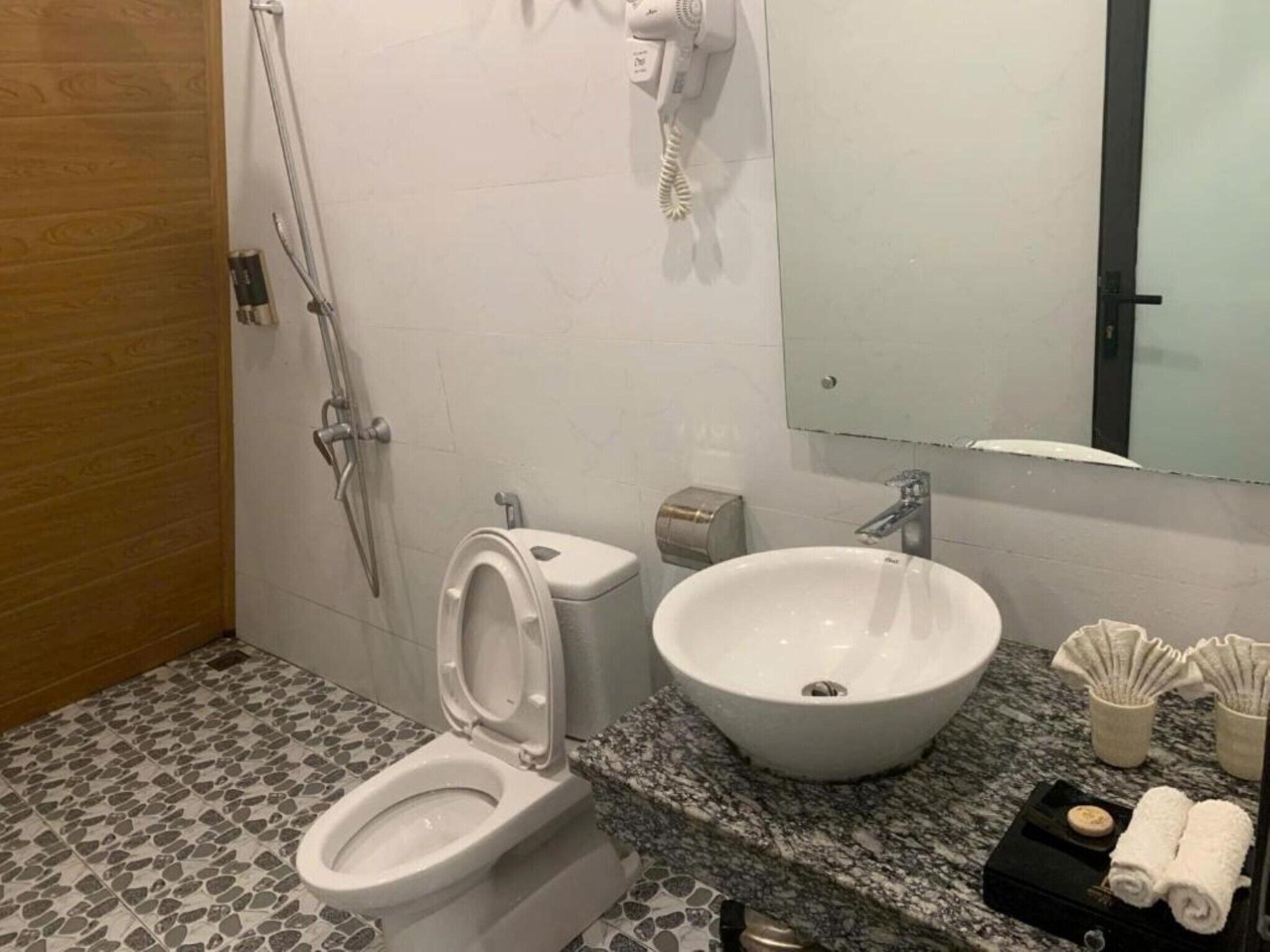 A bathroom with a toilet, bidet, sink, and a hairdryer mounted on the wall.