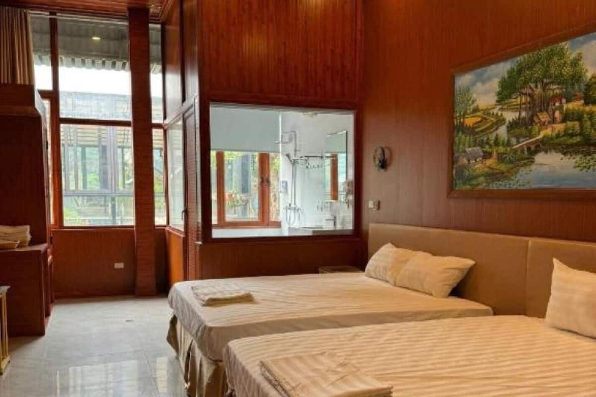 Hotellihuone, jossa on kolme sänkyä, puupanelointi, suuri ikkuna ja taulu seinällä.