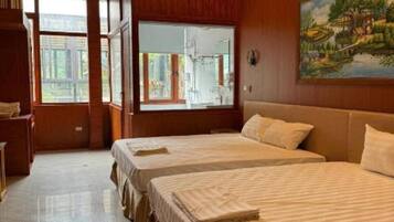 A hotel room with three beds, wooden paneling, a large window, and a painting on the wall.