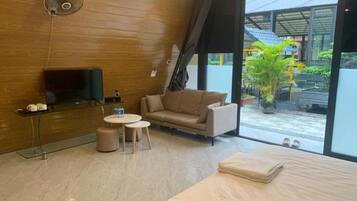 Ein modernes Hotelzimmer mit einem großen Bett, einem Fernseher, einer Couch, zwei kleinen Tischen und einem Deckenventilator.