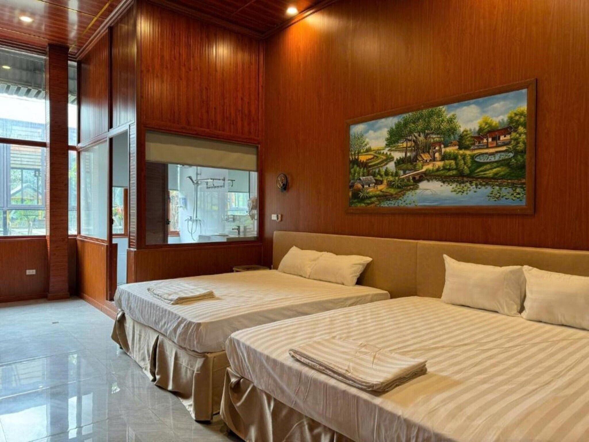A hotel room with two beds, wooden paneling, a large window, and a painting of a landscape.