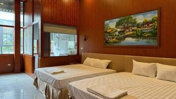 A hotel room with two beds, wooden paneling, a large window, and a painting of a landscape.