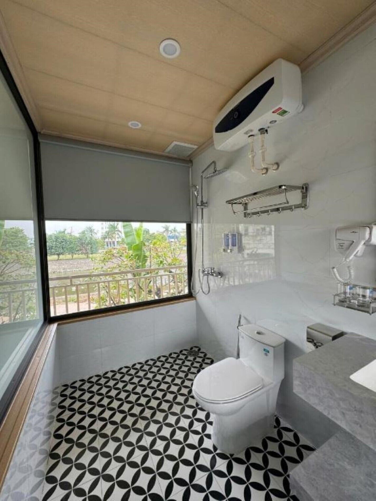 A modern bathroom with a toilet, sink, and shower. It features a geometric patterned floor and a view of greenery outside.