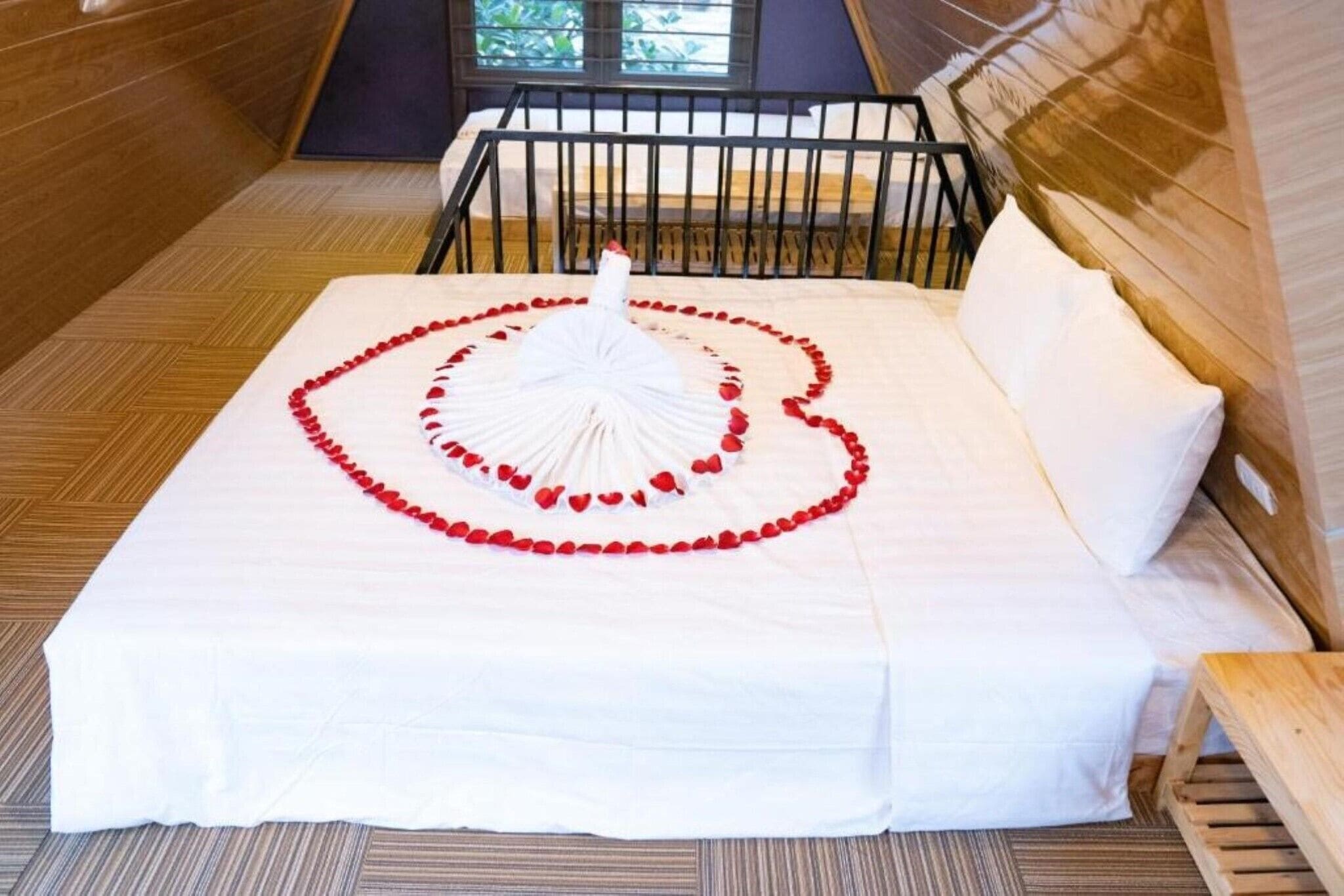 Een bed met een witte spreideken en een hartvormige decoratie van rode rozenblaadjes.