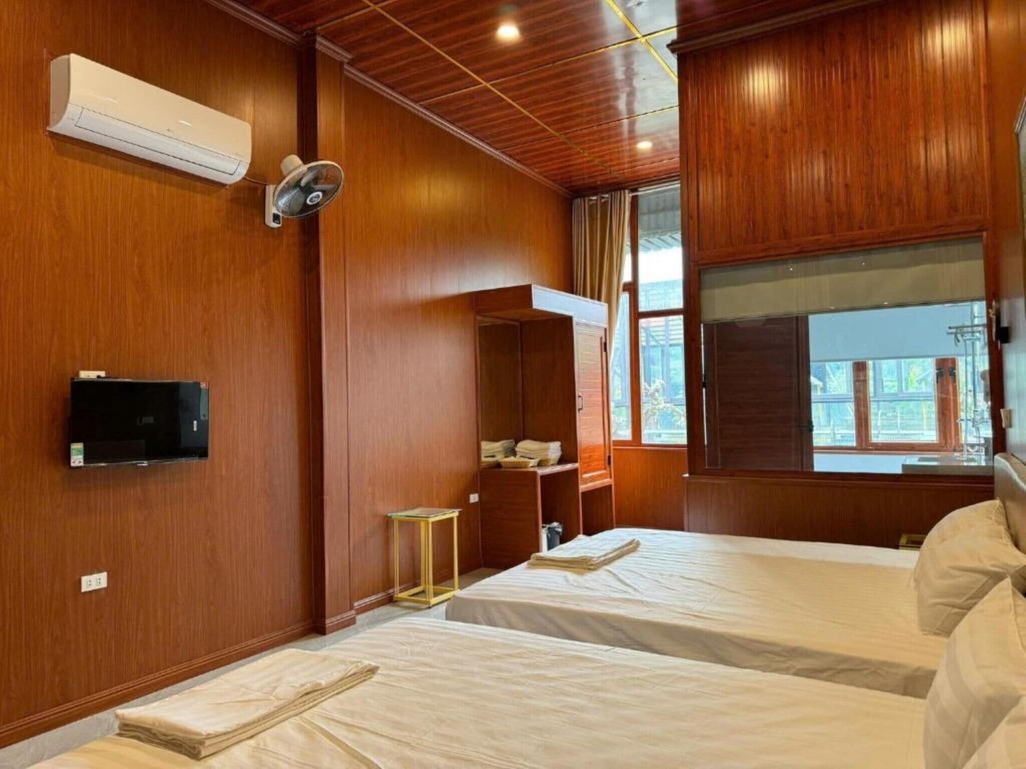 A hotel room with wooden paneling, a bed, a bedside table, a TV, and a window.