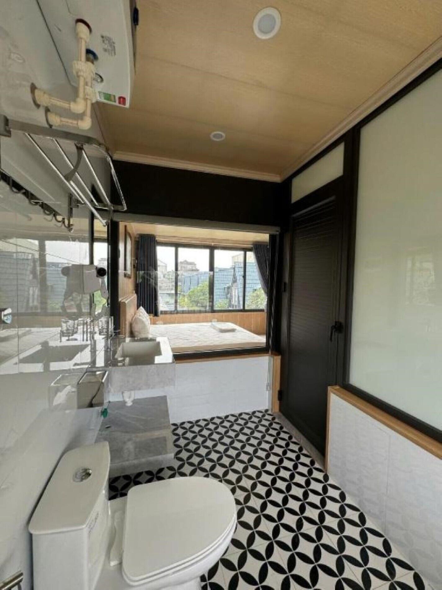 A modern bathroom with a geometric patterned floor, a white toilet, and a large window offering a view of the city.
