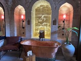 A spa room with a large copper bathtub, a wooden chair, and a wall with a textured design.