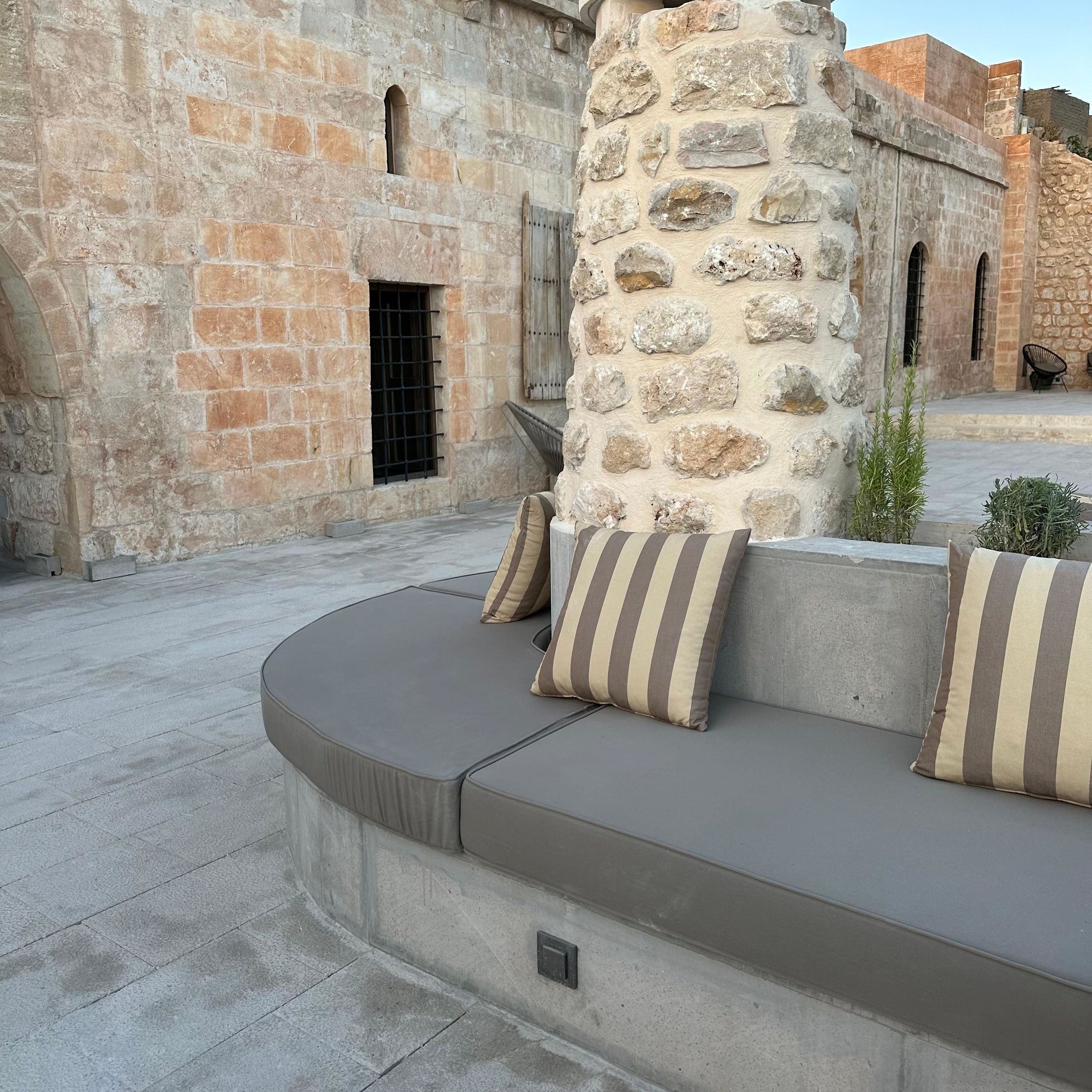 A stone pillar with a cushion bench and a small plant.
