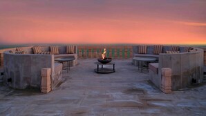Una terraza en la azotea con una chimenea, zona de estar y vistas al océano al atardecer.