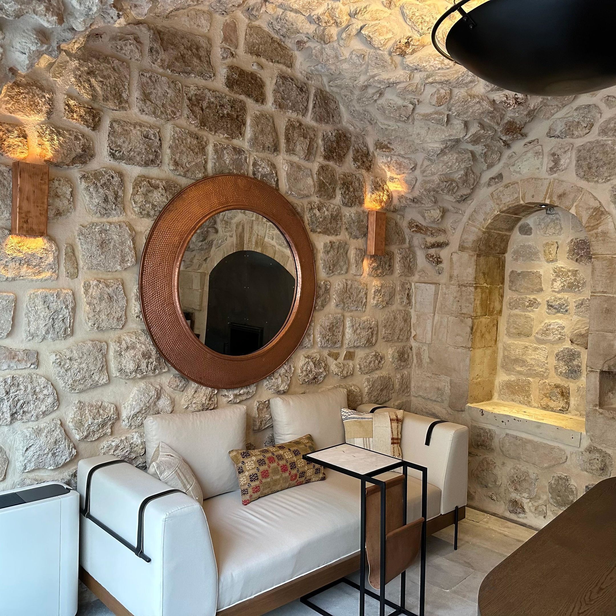 A stone-walled room with a round mirror, two sofas, and a small table.
