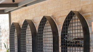 Un restaurante con mesas redondas y sillas de madera, una pared de piedra y una valla metálica con botellas al fondo.