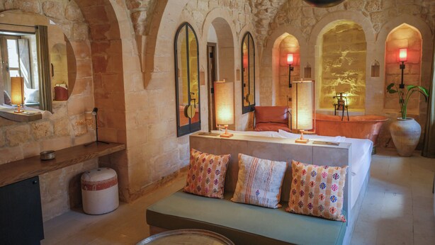 Una habitación acogedora con pared de piedra, un sofá con cojines estampados, una mesa redonda y un espejo.