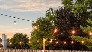 A backyard with a fire pit, two Adirondack chairs, and string lights.