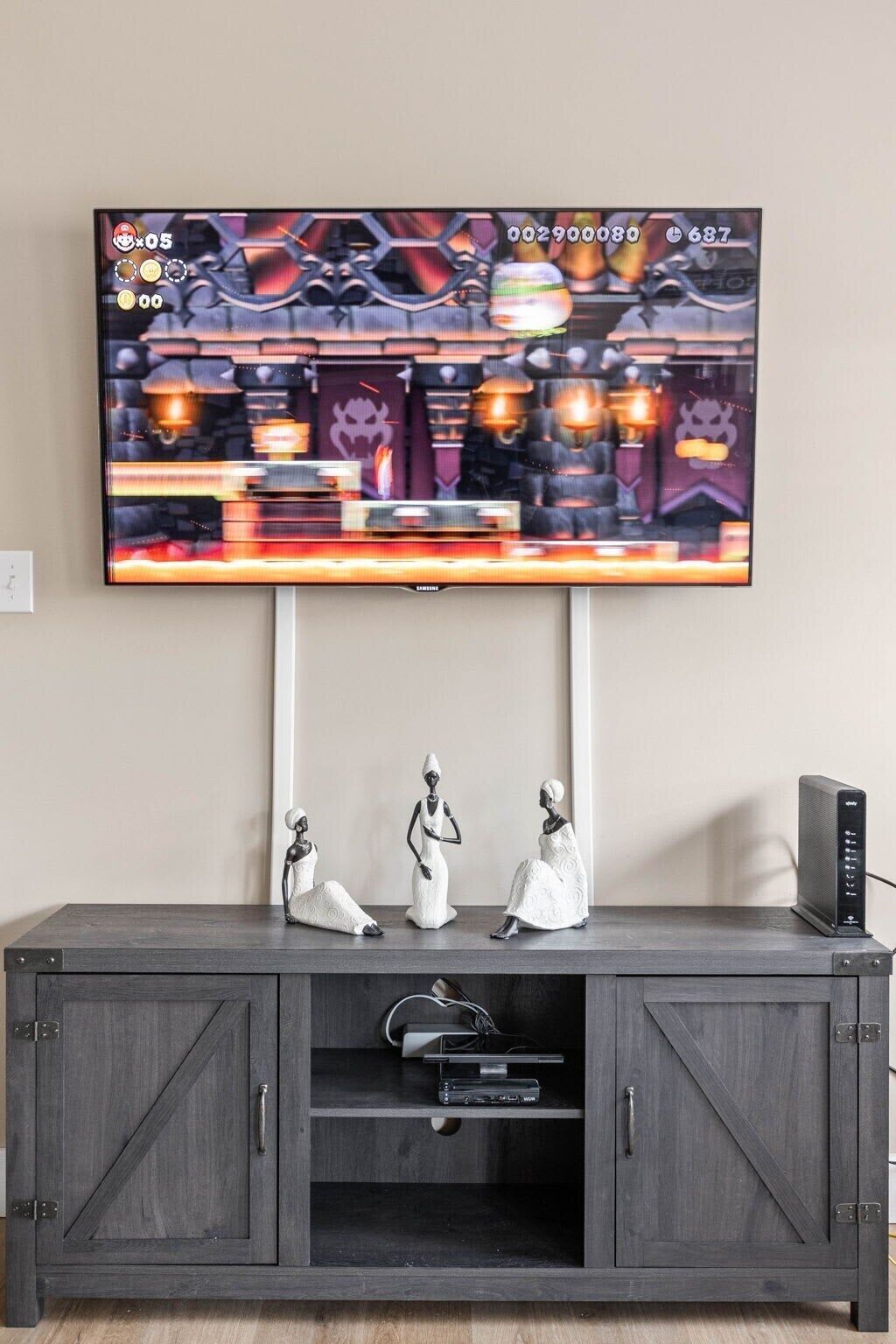 A television mounted on a wall above a dark wooden cabinet with decorative figurines and a speaker.