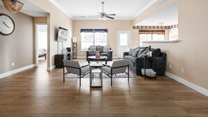 A spacious living room with a ceiling fan, a dining area with a round table and chairs, and a dark-colored sofa.