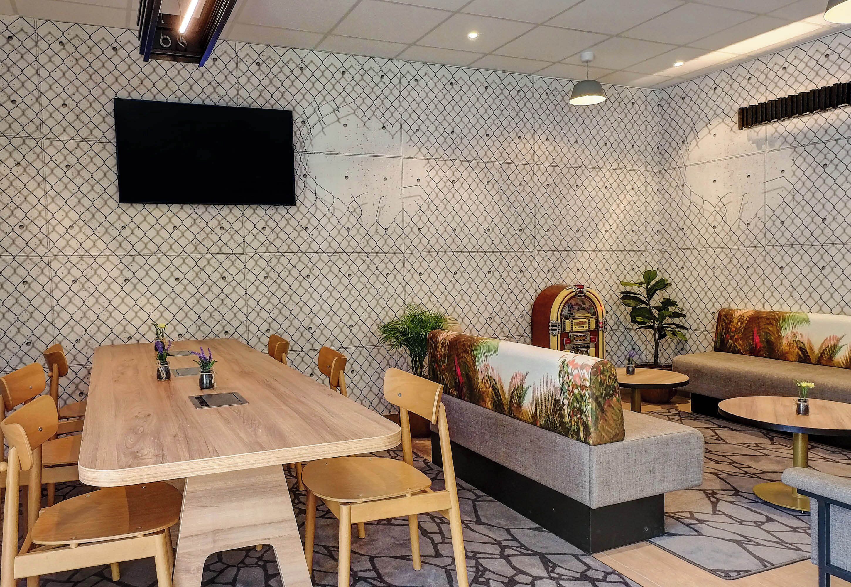 A conference room with a long wooden table, several chairs, a sofa, and a TV mounted on the wall.
