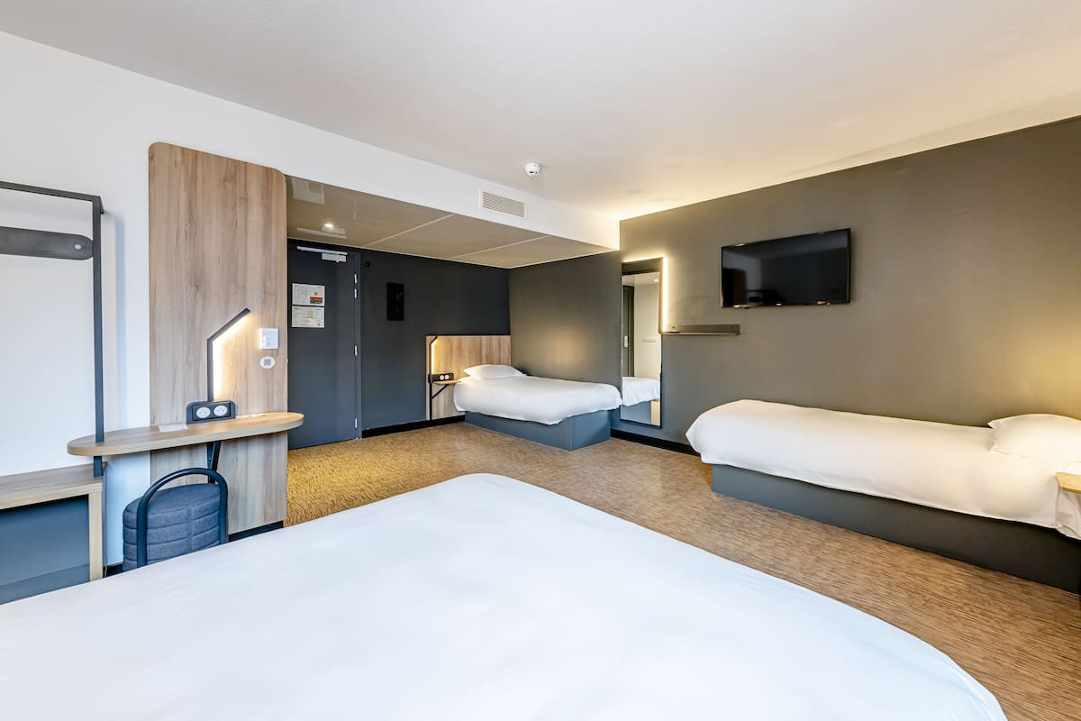 Ein Hotelzimmer mit zwei Betten, einem Schreibtisch, einem Stuhl, einem Fernseher und einem Spiegel.
