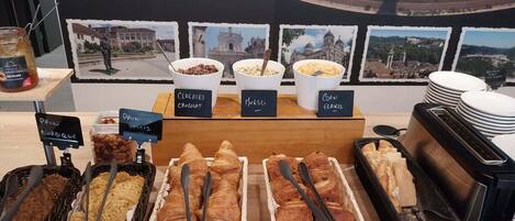 Un bufé de desayuno con tazones de cereales etiquetados, una selección de pasteles y una estación de café.