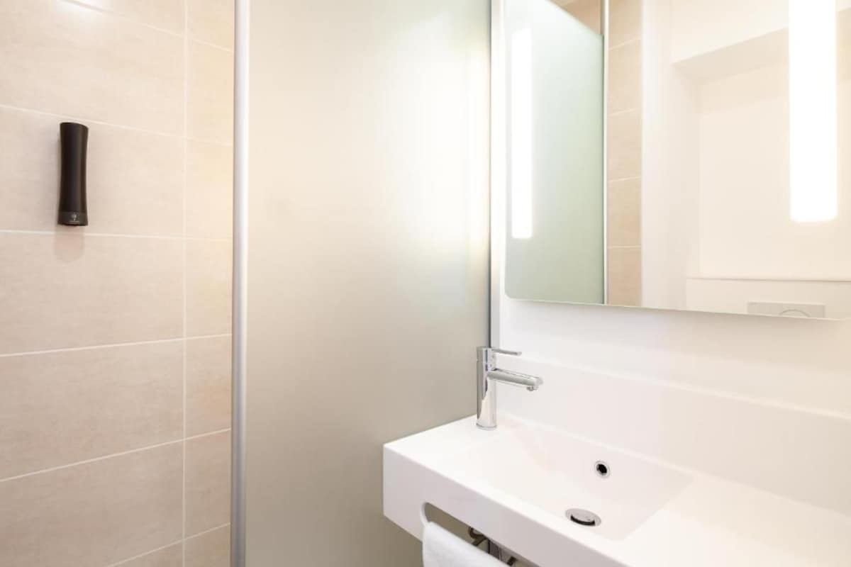A modern bathroom with a white sink, a mirror, and a shower area.
