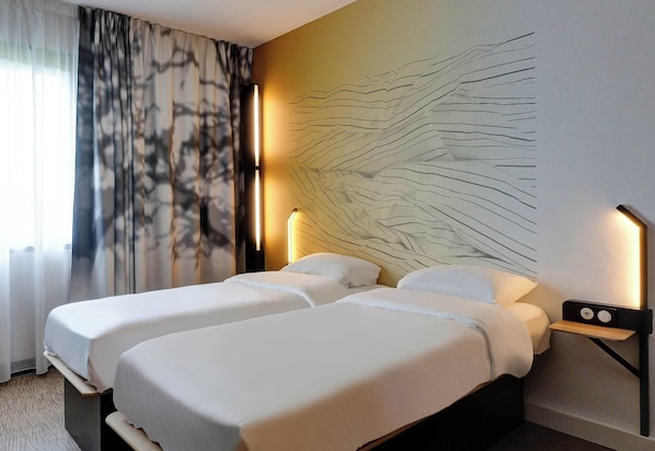 A hotel room with two beds, a large abstract wall art, a nightstand with a lamp, and a view of the outdoors through sheer curtains. - B&B HOTEL Besançon Valentin (Miserey-Salines)