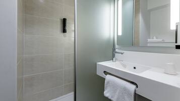 Un baño moderno con cabina de ducha de vidrio, un lavabo blanco y un espejo grande.