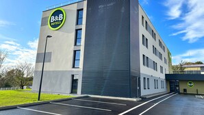 A B&B hotel building with a modern design, featuring a large sign on the facade and a parking lot in front. - B&B HOTEL Besançon Valentin (Miserey-Salines)