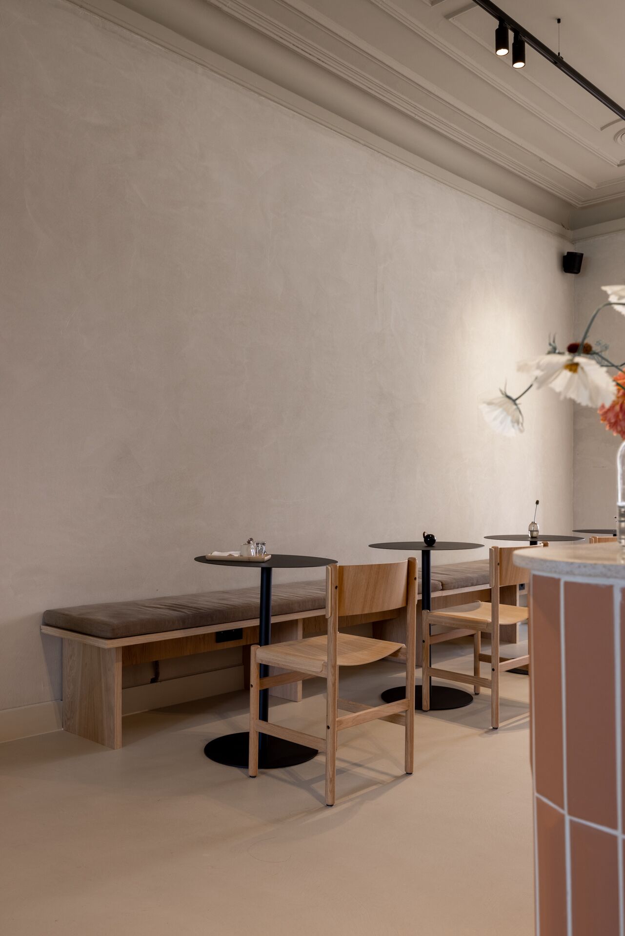 A minimalist interior with wooden benches and tables, a vase with flowers, and a ceiling track lighting system.