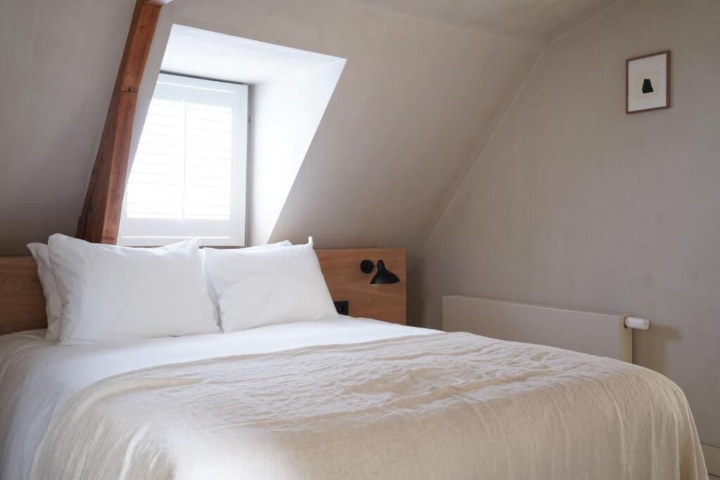 A bedroom with a sloped ceiling, a large window, a wooden headboard, and a bedside lamp.