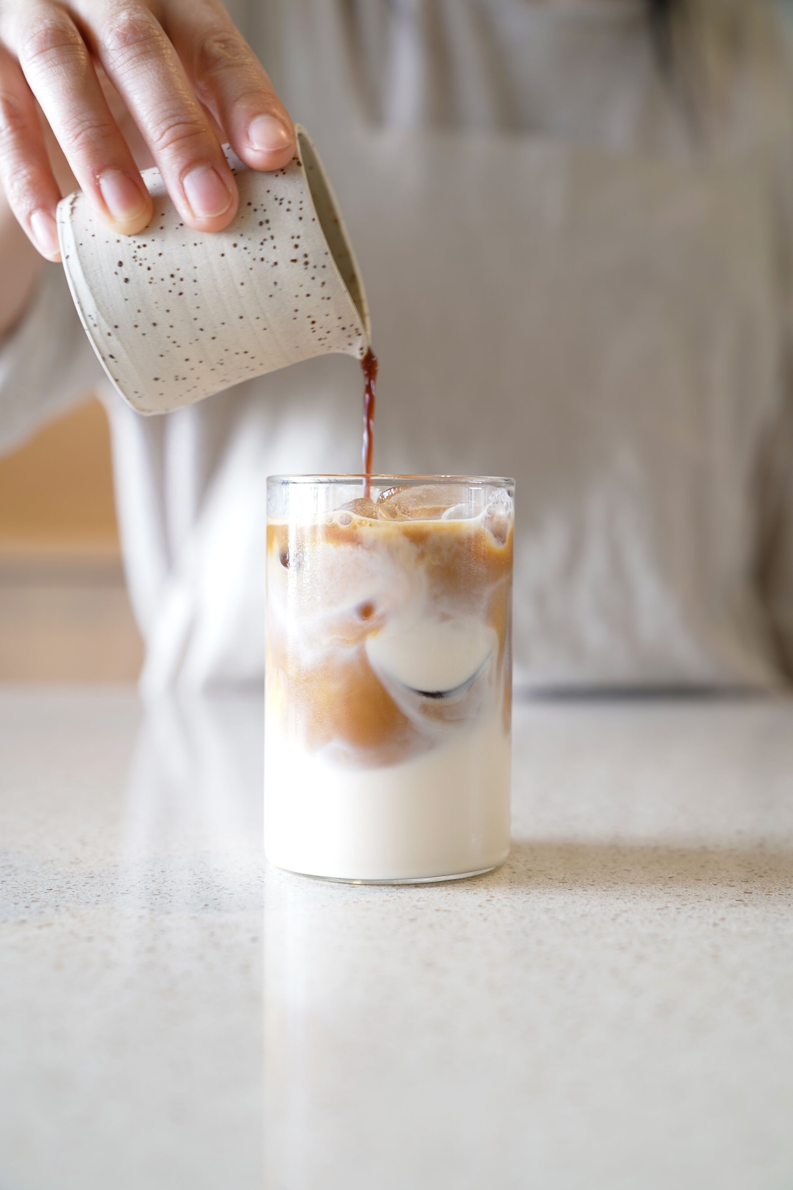 A hand pouring a beverage into a glass with ice and milk.