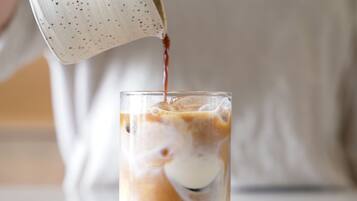 A hand pouring a beverage into a glass with ice and milk.