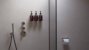 A bathroom with a shower, three bottles of shampoo, and a toilet paper holder.