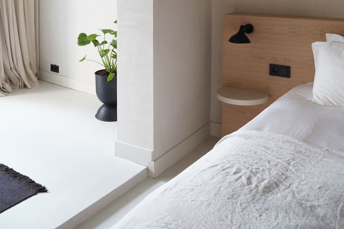 Un dormitorio moderno con una cama grande, una mesita de noche, una planta en maceta y vistas al exterior.