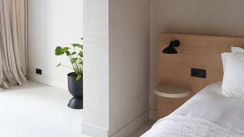 Une chambre à coucher moderne avec un grand lit, une table de chevet, une plante en pot et une vue sur l’extérieur.