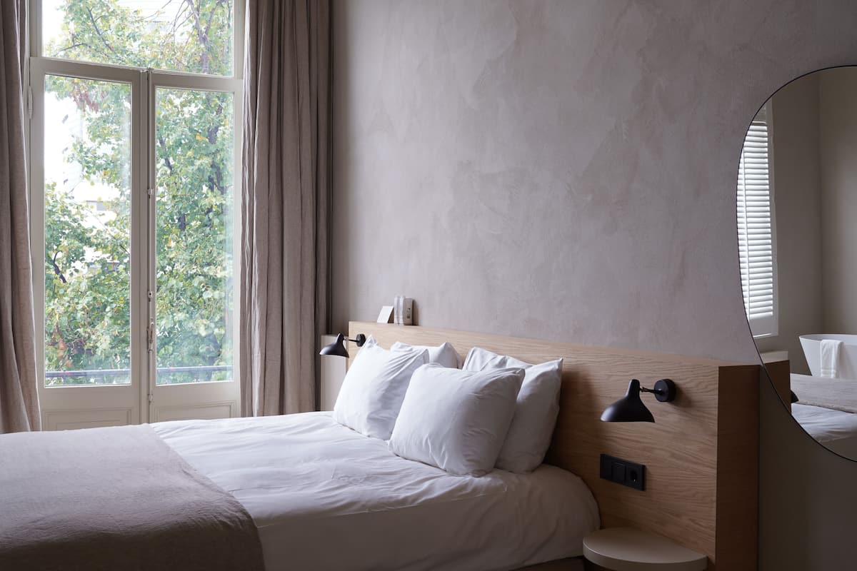 Una habitación de hotel con una cama grande, un espejo redondo, una mesita de noche y vistas a árboles desde la ventana.