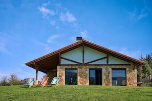 Une maison moderne avec une façade en pierre, de grandes fenêtres et un toit en pente.