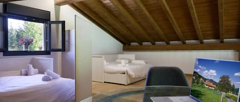 Een slaapkamer met een bed, een bureau met een laptop en een raam met uitzicht op groen.