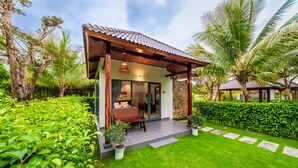 A modern house with a covered porch, a dining area, and a well-maintained garden with palm trees and shrubs. - Emerald Garden Retreat (Phu Quoc)