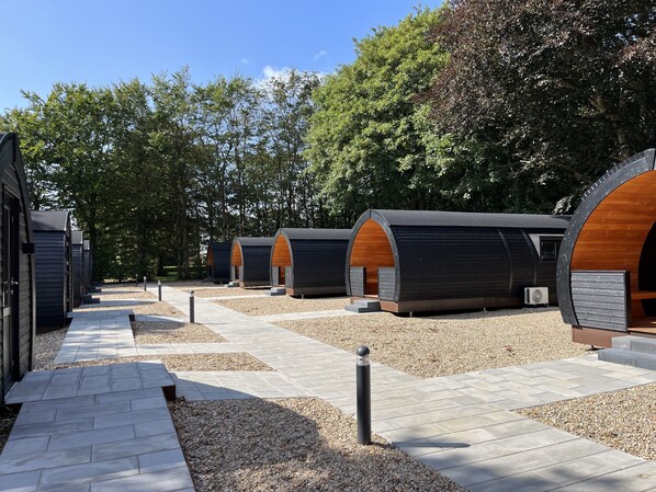 A row of modern, arched cabins with a gravel pathway leading to them, surrounded by trees. - Helle Aktivitetshotel (Arre)
