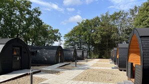 A row of modern, semi-circular wooden cabins with a gravel pathway between them. - Helle Aktivitetshotel (Arre)