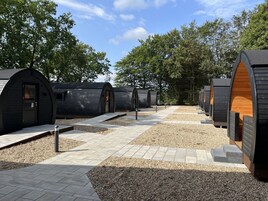 Uma fileira de cabanas de madeira modernas e semicirculares, com um caminho de cascalho entre elas.
